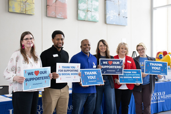 Practicum directors and advisors hold signs that thank donors for their support on One Day One KU